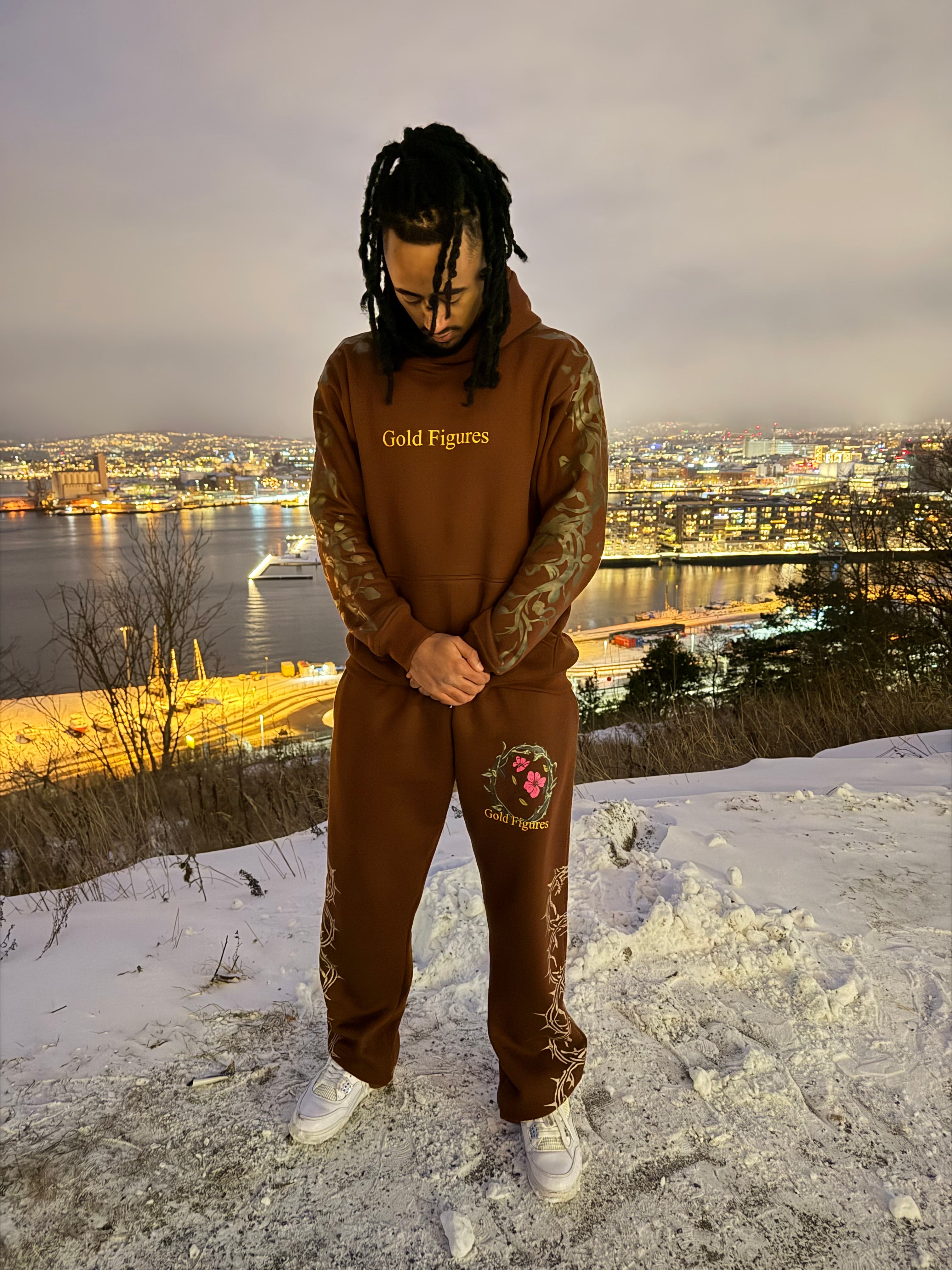 Person wearing a brown hoodie and pants with floral design, standing on a snowy surface.